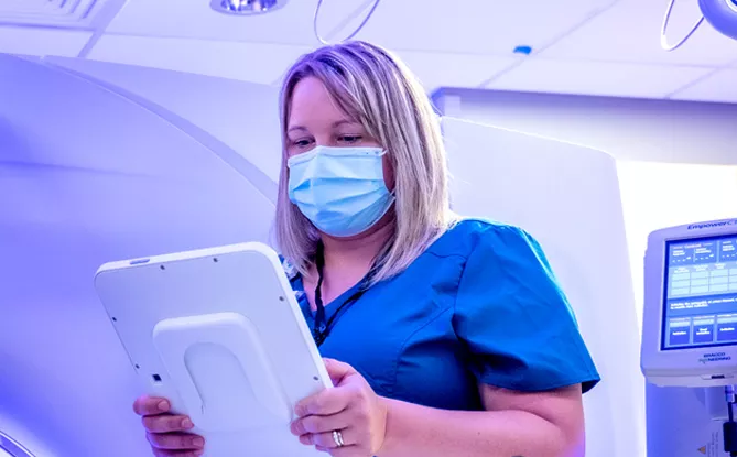 Nurse wearing scrubs and a medical mask reading results from a computer screen